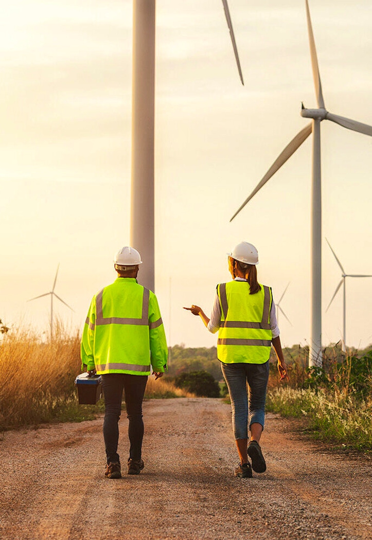 Construction workers walking on a path surrounded by wind turbines