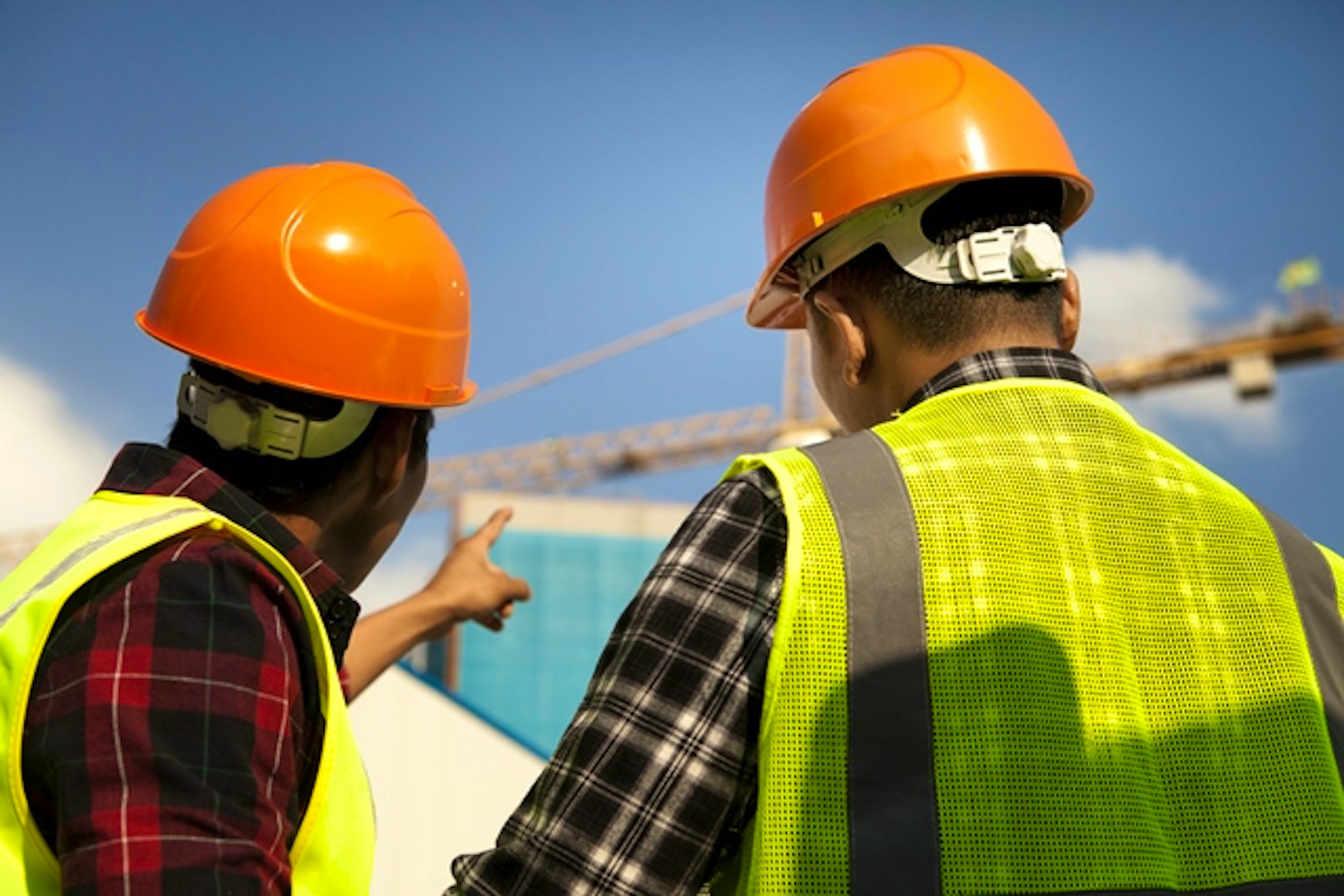 Two construction workers pointing towards a crane
